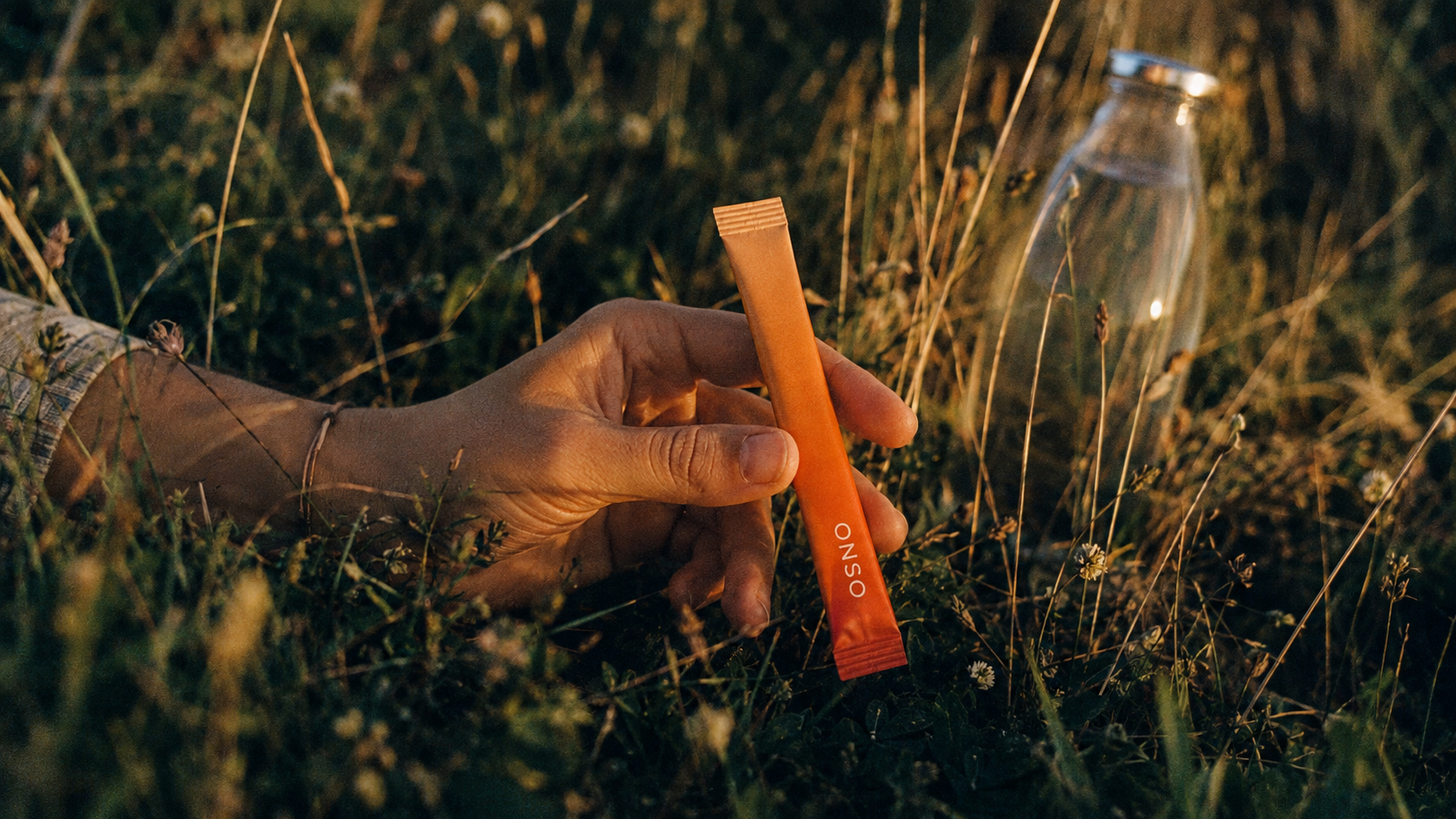 Hand holding an ONSO caffeine stick in warm afternoon grass