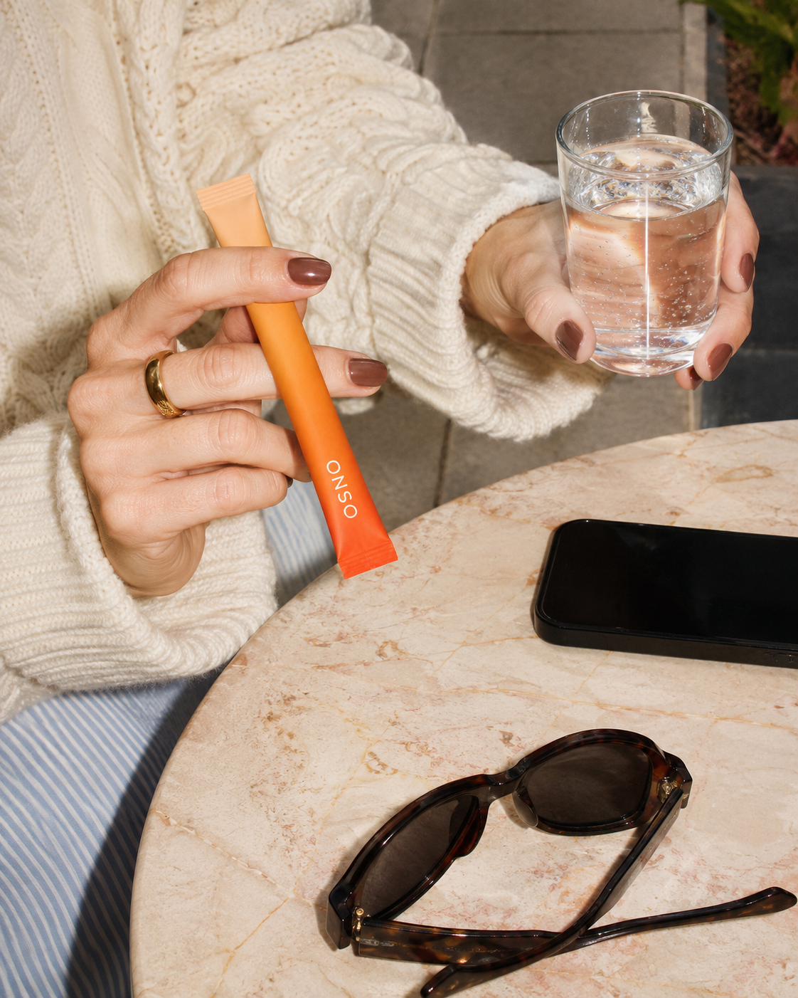 A hand holding an ONSO stick next to a glass of water